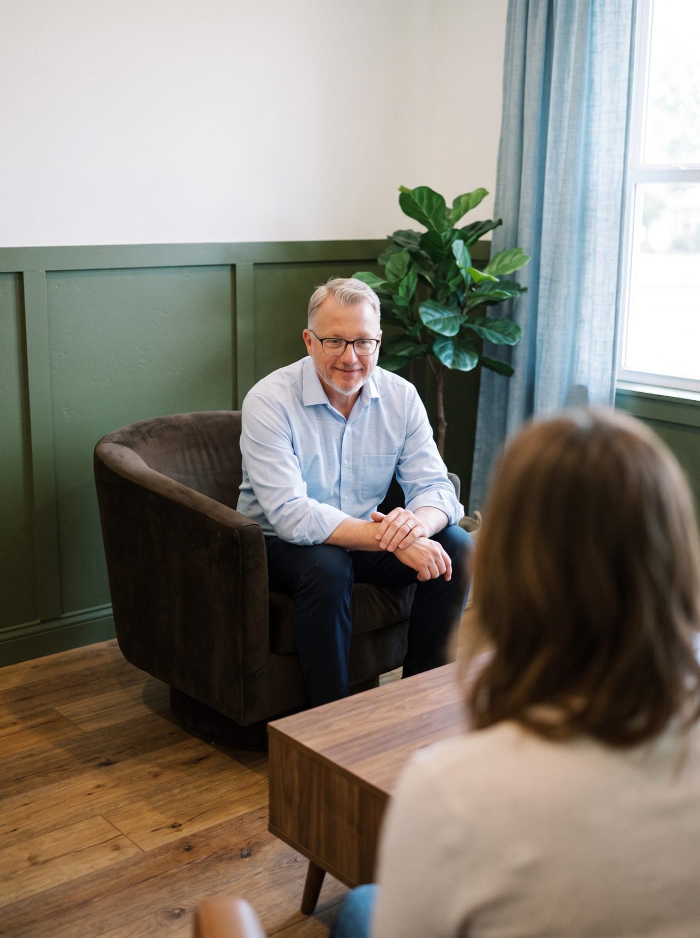 Dr. Nelson in an armchair, listening to a patient across a coffee table.